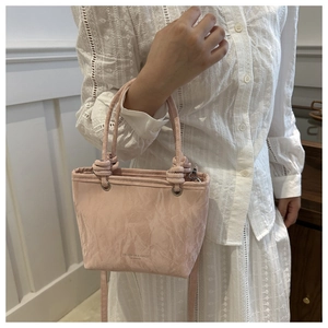 Gros plan du sac seau rose en cuir plissé avec poignée nouée et détails en argent