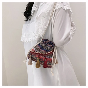 Détail d'un sac seau tissé bohème avec glands colorés sur robe en dentelle blanche