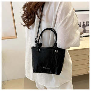 Détail du sac seau noir texturé avec logo blanc porté par un mannequin vêtu de blanc