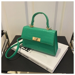 Détail du sac en cuir crocodile vert avec un fermoir rotatif doré posé sur un livre
