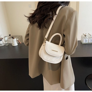 Detail of white mini saddle bag showing pleated faux leather texture and golden metal bar