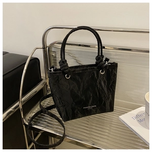 Détail du sac seau trapèze noir avec texture froissée brillante et poignées à nœuds