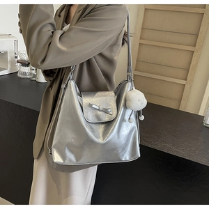 Silver metallic tote bag with bow detail and plush charm shown on person in cafe