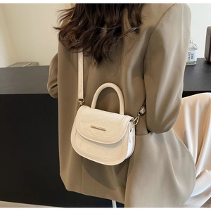 Detail of a creamy white pleated leather saddle bag with gold metal buckle and handle