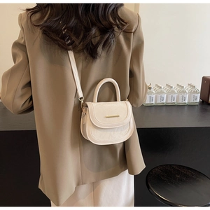 Rear view of a minimalist cream saddle bag with gold metal buckle on a brown suit