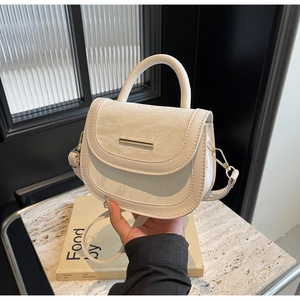 Close-up of cream white saddle bag featuring vintage crinkled leather and gold metal trim