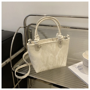 Détail d'un sac cabas plissé crème avec poignée nouée sur un présentoir argenté