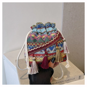 Détail du sac seau tissé avec des motifs colorés et de longs pompons décoratifs