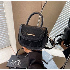Detail of black saddle bag featuring a marble pattern flap and gold metal hardware