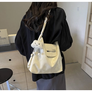 Detail of beige soft leather tote bag with bow design and plush cloud charm on shoulder