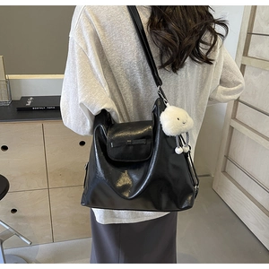 Detail of glossy black tote bag featuring a cute white plush cloud charm and flap closure