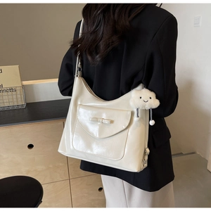 Detail of cream white tote bag with front bow pocket and plush cloud charm accessory
