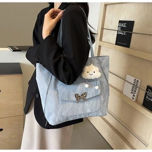 Detail view of light blue pleated tote bag with metal butterfly buckle and plush charm