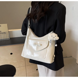 Detail view of large cream tote bag with bow pocket and cloud charm on a model shoulder