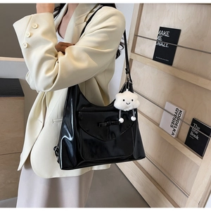 Glossy black tote bag with bow detail and white cloud plush charm in a lifestyle setting