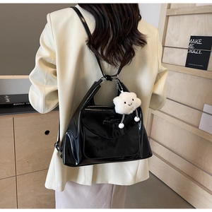 Detail of glossy black flap backpack featuring a soft white cloud plush pendant charm