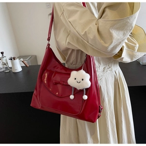 Detail of red patent leather tote bag with bow accent and white cloud plush charm