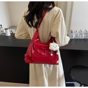 Detail of red glossy leather tote bag featuring a ribbon bow and plush cloud charm