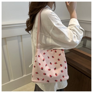 Detail of light pink corduroy bucket bag with embroidered strawberry patterns and thin strap