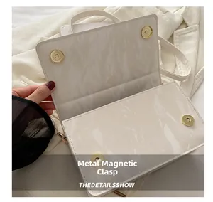 Close-up of golden magnetic buckle on white marble pattern square bag with flap