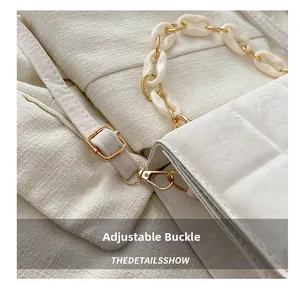 Detail of white quilted handbag with golden adjustable buckle and acrylic deco chain