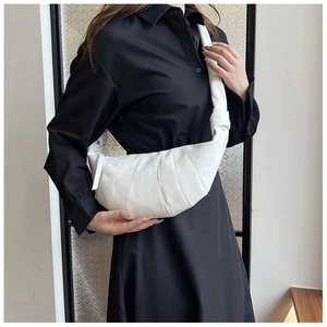 White pleated dumpling bag with wide shoulder strap worn by a model in a black dress