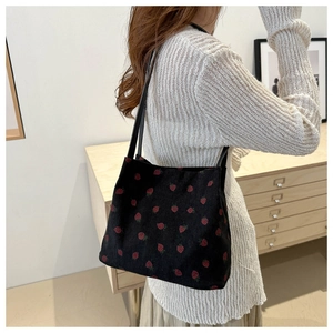 Detail of black corduroy tote bag featuring red strawberry patterns and slim shoulder straps