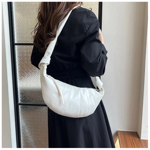 Detail of white faux leather crescent bag featuring pleated design and knotted wide strap