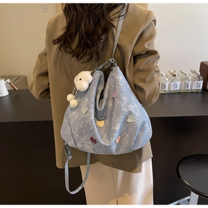 Détail d'un sac cabas en denim bleu clair avec écussons cœurs 3D et breloque en peluche