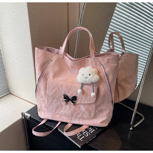 Pink nylon tote bag detail with butterfly buckle and cloud charm on a dark desk