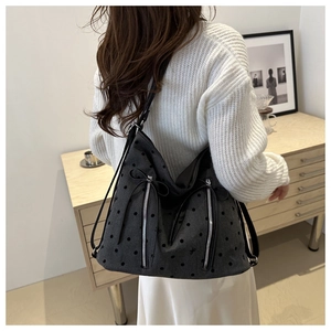 Detail of black polka dot tote bag with silver zippers and bow accents on a model