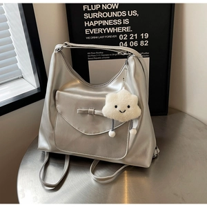 Detail of silver shiny tote bag with bow detail and fluffy cloud charm on a table