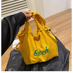 Close-up of bright yellow nylon tote bag with green Beach lettering and drawstring detail