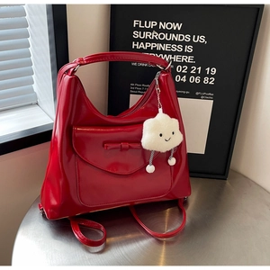 Detail of red glossy patent leather tote bag with bow accent and plush cloud charm