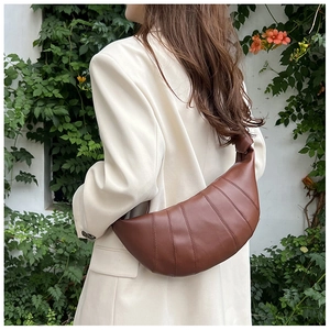 Detail of caramel crescent crossbody bag with stitching and decorative knot on strap
