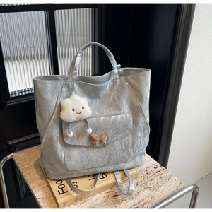 Detail of silver pleated tote bag featuring a gold butterfly buckle and plush charm
