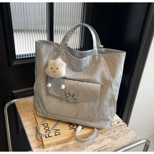 Detail of silver crinkled tote bag featuring a metal butterfly and plush cloud charm