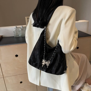 Black pleated tote bag with silver butterfly pendant and metal chain on model shoulder
