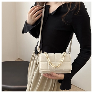 Detail of a beige quilted crossbody bag with a thick decorative chain and adjustable strap