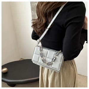 Silver quilted crossbody bag with designer acrylic chain worn by a model in modern interior