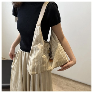 Detail view of cream pleated shoulder bag with dark drawstring and amber bead accessory