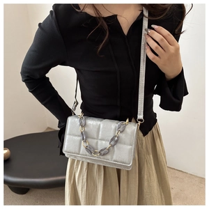 Detail of silver grey quilted crossbody bag with decorative acrylic and metal chain