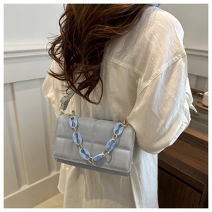 Detail of light blue quilted crossbody bag featuring resin and gold chain strap