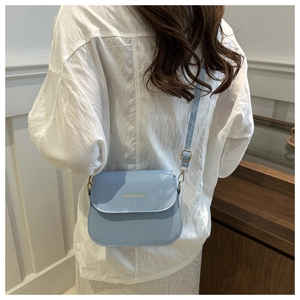 Detail of light blue PU leather saddle bag with gold hardware worn over a white shirt