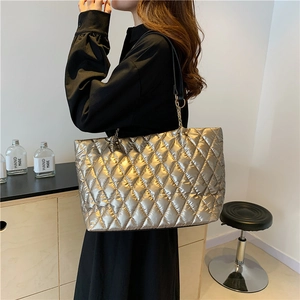 Quilted champagne gold tote bag with chain strap shown on model in a modern room