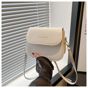 Close-up of white saddle bag with gold FASHION & BAGS lettering and leather strap