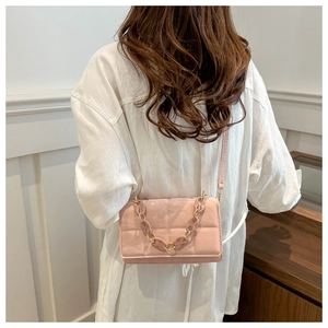 Detail of pink quilted square crossbody bag with stylish resin chain worn by model