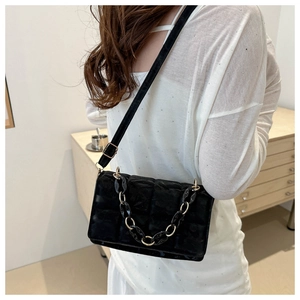 Detailed view of black quilted crossbody bag with chunky chain on model shoulder
