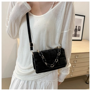 Detail of black quilted velvet crossbody bag with bold chain on a dressed-up model