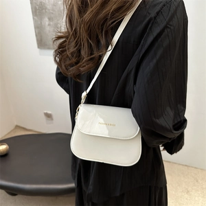 Minimalist beige glossy square crossbody bag with gold lettering shown on model